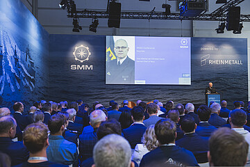 Teilnehmende verfolgen die Keynote von Vizeadmiral Jan Christian Kaack auf der Konferenzbühne der SMM. Auf einer großen Leinwand werden Präsentationsinhalte gezeigt.