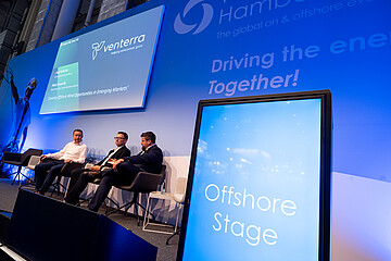 Podiumsdiskussion auf der Offshore Stage einer Fachmesse. Mehrere Branchenvertreter tauschen sich auf der Bühne über Chancen und Entwicklungen im Offshore-Windenergiemarkt aus.