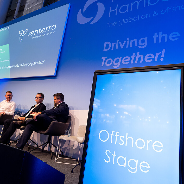 Podiumsdiskussion auf der Offshore Stage einer Fachmesse. Mehrere Branchenvertreter tauschen sich auf der Bühne über Chancen und Entwicklungen im Offshore-Windenergiemarkt aus.