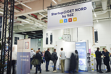 Besucherinnen und Besucher informieren sich an Messeständen im Startup-Bereich der GET NORD. Über dem Ausstellungsbereich weist ein großes Banner auf „Startup@GET NORD by VdZ“ hin. Die Aufnahme zeigt das Messegeschehen in einer hell beleuchteten Halle.