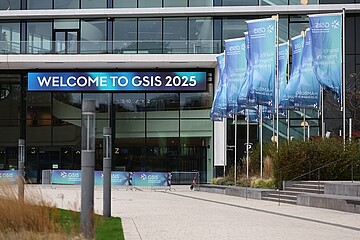 Eingangsbereich des modernen Congress Center Hamburg (CCH) mit einem großen digitalen Banner, auf dem ‚Welcome to GSIS 2025‘ steht. Rechts auf dem Vorplatz wehen mehrere blau‑türkise GSIS-Flaggen.
