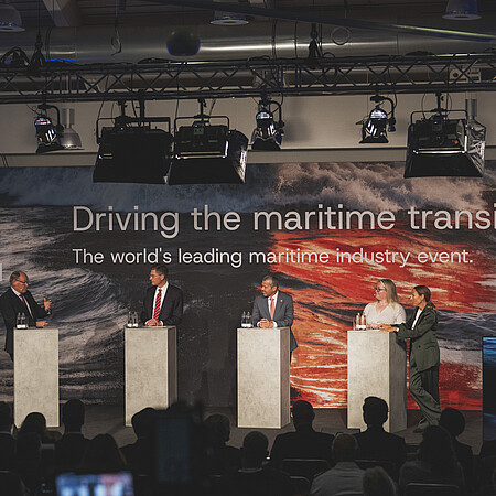Podiumsdiskussion auf der SMM vor Publikum. Mehrere Sprecherinnen und Sprecher stehen auf einer Bühne vor einer großformatigen Veranstaltungswand zum Thema maritime Transformation.